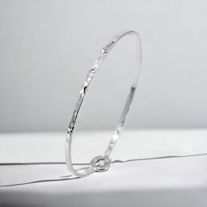 May include: A silver hammered bangle bracelet. The bracelet is thin and has a smooth, polished finish.