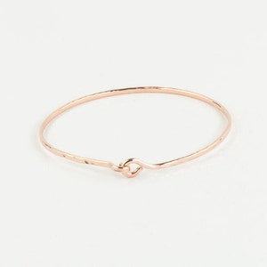 May include: A delicate rose gold bangle bracelet with a hammered finish and a simple, open loop closure.