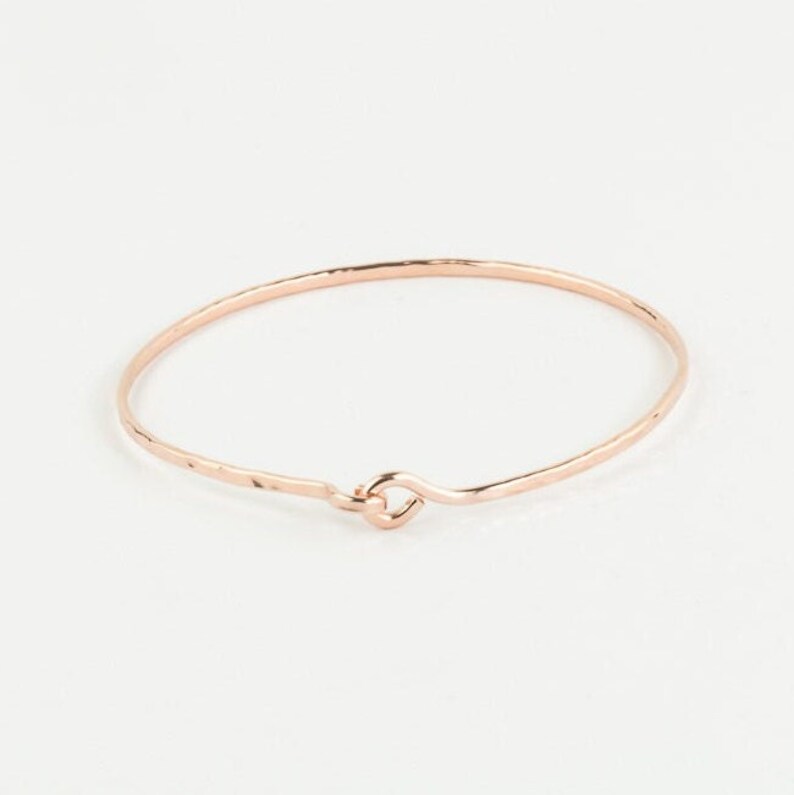 May include: A delicate rose gold bangle bracelet with a hammered finish and a simple, open loop closure.