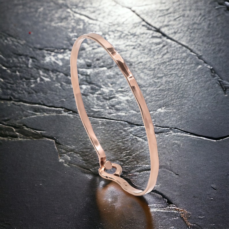 May include: A rose gold hammered bangle bracelet with a simple, minimalist design.