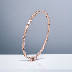May include: A rose gold bangle bracelet with a delicate wire design. The bracelet is made of hammered metal and has a simple clasp.
