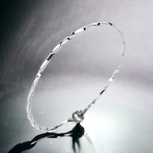 May include: A silver twisted bangle bracelet. The bracelet is made of a thin, flexible metal and has a smooth, polished finish.