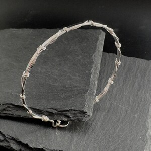 May include: A silver bangle bracelet with a twisted wire design. The bracelet is made of two different thicknesses of wire, creating a unique and textured look.