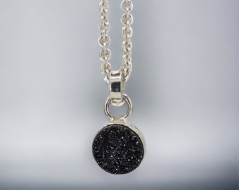 May include: A silver chain necklace with a round black pendant. The pendant is made of a textured black material.