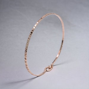 May include: A delicate rose gold bangle bracelet with a textured surface. The bracelet has a simple, elegant design and is perfect for everyday wear.