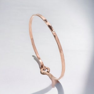May include: A simple, hammered rose gold bangle bracelet with a smooth, polished finish.