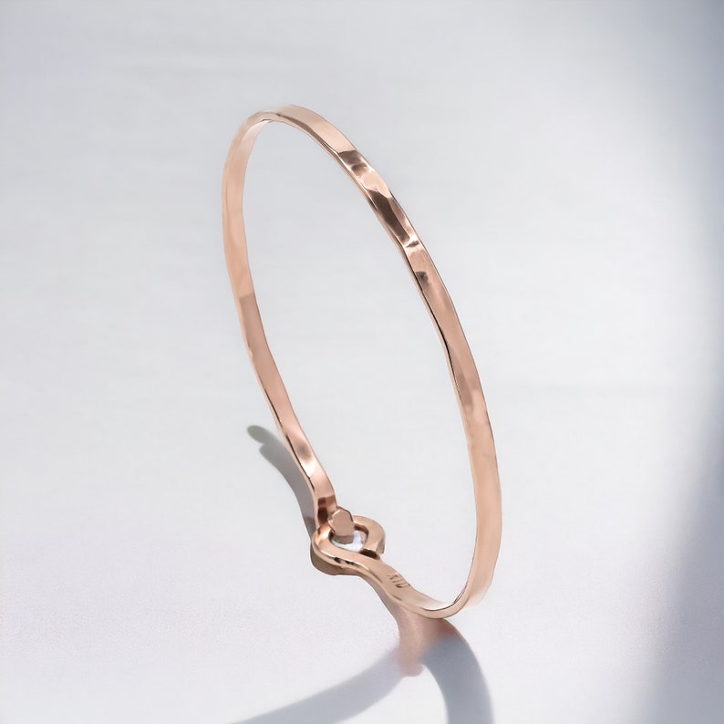 May include: A simple, hammered rose gold bangle bracelet with a smooth, polished finish.