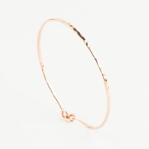 May include: A delicate rose gold hammered bangle bracelet. The bracelet is thin and has a simple, elegant design.