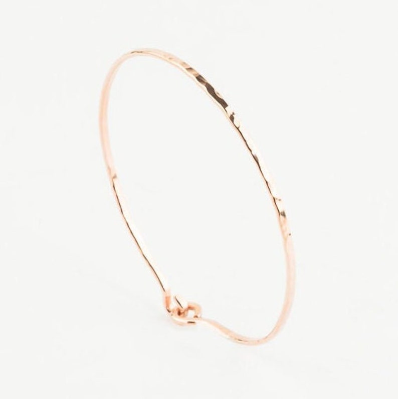 May include: A delicate rose gold hammered bangle bracelet. The bracelet is thin and has a simple, elegant design.
