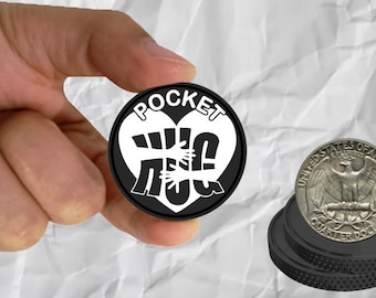 May include: A black and white pocket-sized phone stand with the text "POCKET PUG" and a heart with two hands inside. The stand is being held in a hand.