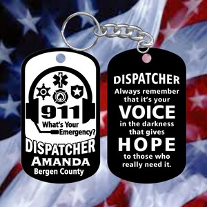 May include: Black and white keychain with a 911 dispatcher design. The front side features a headset with a 911 logo and the text "What's Your Emergency?" The back side features the text "Dispatcher Always remember that it's your voice in the darkness that gives hope to those who really need it."