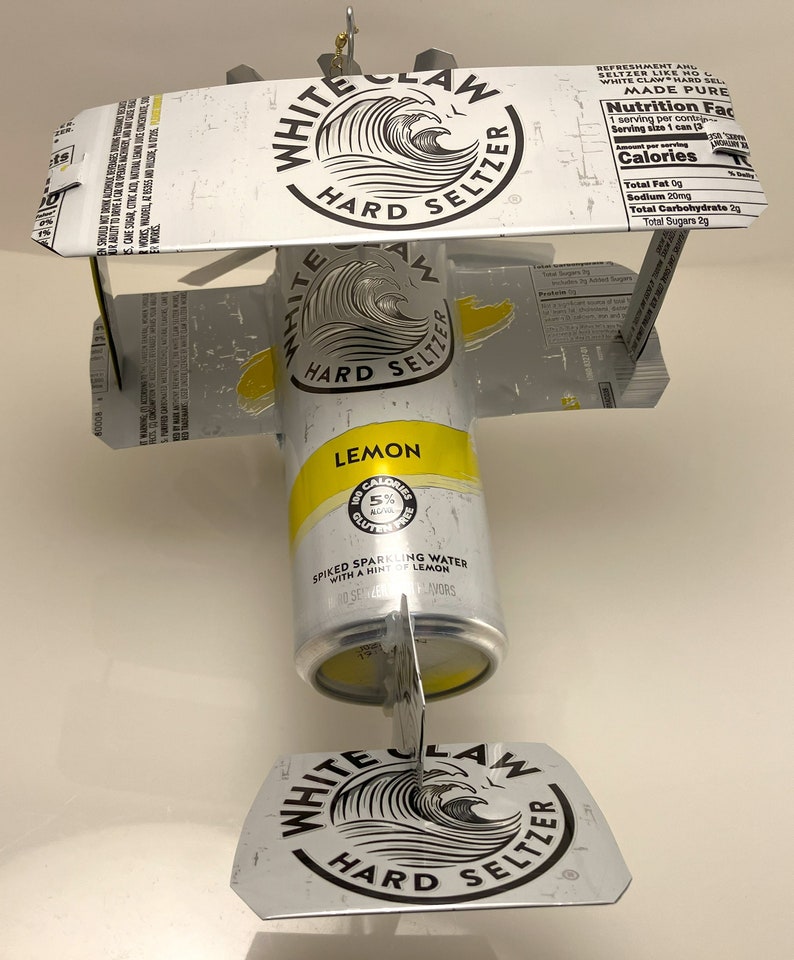 K&ouml;nnte beinhalten: Eine White Claw Hard Seltzer Dose mit Zitronengeschmack, die in ein Modellflugzeug verwandelt wurde. Die Dose ist gelb mit schwarzem Text und einem Wellendesign. Die Fl&uuml;gel und der Schwanz sind aus dem oberen und unteren Teil der Dose gefertigt.
