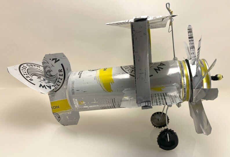 K&ouml;nnte beinhalten: Ein Modellflugzeug aus einer silbernen Dose White Claw Hard Seltzer Lemon. Die Fl&uuml;gel sind aus dem Etikett der Dose und der Propeller aus der Oberseite der Dose gefertigt. Das Flugzeug hat schwarze R&auml;der und einen Draht-Heck.