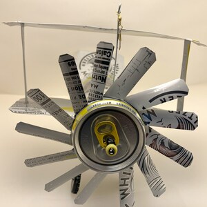 K&ouml;nnte beinhalten: Ein Modellflugzeug aus Aluminiumdosen. Die Fl&uuml;gel sind aus den Seiten der Dosen und der Rumpf aus der Oberseite der Dose. Das Flugzeug hat einen Propeller und einen Schwanz.
