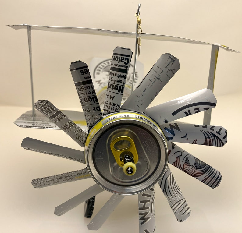 K&ouml;nnte beinhalten: Ein Modellflugzeug aus Aluminiumdosen. Die Fl&uuml;gel sind aus den Seiten der Dosen und der Rumpf aus der Oberseite der Dose. Das Flugzeug hat einen Propeller und einen Schwanz.
