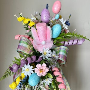 May include: A white lantern decorated with pastel pink, purple, blue, and yellow Easter eggs, flowers, and ribbon. The lantern is filled with more Easter eggs.