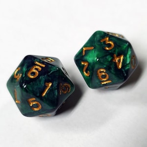May include: Two green and gold polyhedral dice. The dice are a deep emerald green with gold numbering. The dice are used for tabletop games and role-playing games. The dice are set against a white background.
