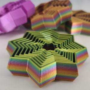 May include: A multi-layered star-shaped cookie cutter with a rainbow color gradient. The cutter is made of green plastic and has a series of concentric rings.