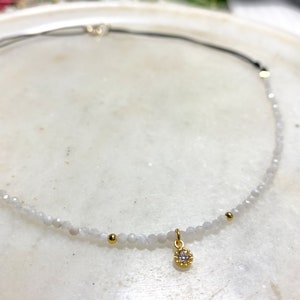 Moonstone choker really tiny and delicate in a white marble plate, you can see the different parts of the choker, half with moonstone and a small  gold cz charm in the middle and the back part maded with black nylon thread