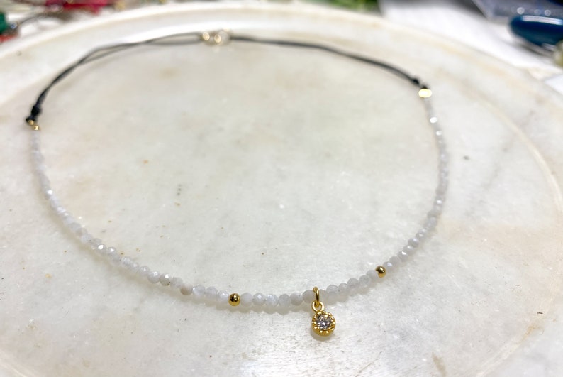 Moonstone choker really tiny and delicate in a white marble plate, you can see the different parts of the choker, half with moonstone and a small  gold cz charm in the middle and the back part maded with black nylon thread