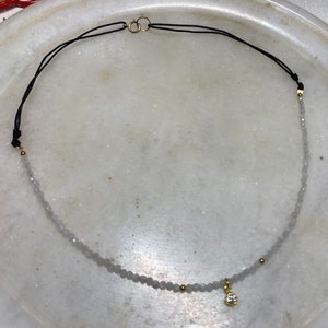 Moonstone choker really tiny and delicate in a white marble plate, you can see the different parts of the choker, half with moonstone and a small  gold cz charm in the middle and the back part maded with black nylon thread