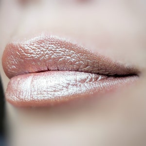 May include: Close-up of a person's lips, coated in a shimmering, metallic lipstick. The color is a blend of bronze and silver, creating a pearlescent effect. The texture of the lipstick is visible, highlighting the lip's natural lines.