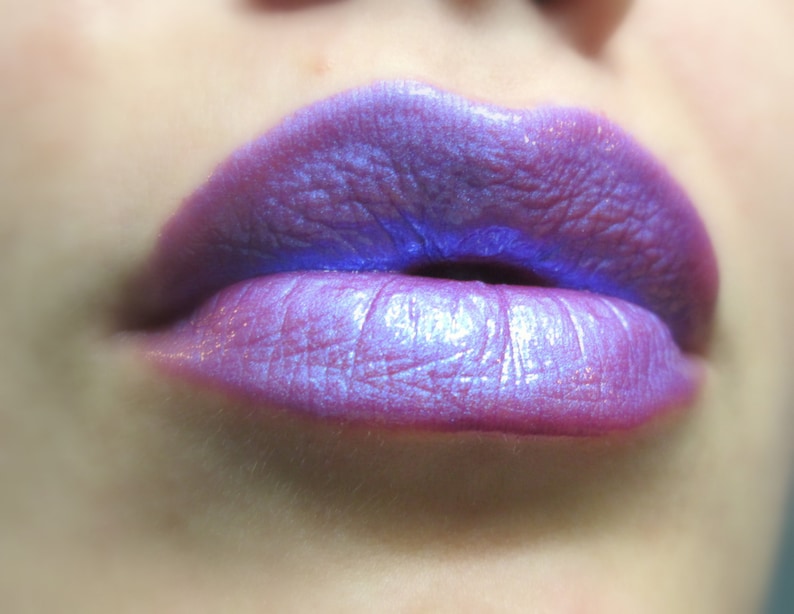 May include: Close-up of a person's lips wearing a shimmery purple lipstick with a blue undertone.