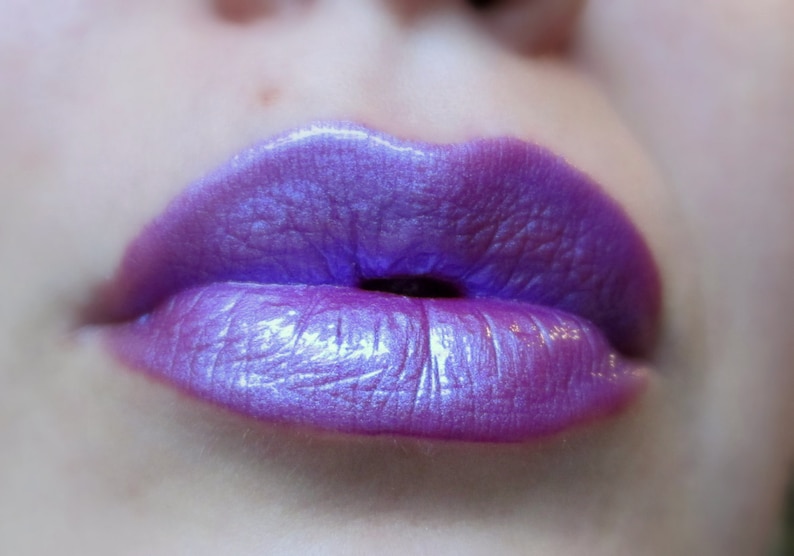 May include: Close-up of a person's lips wearing a shimmery purple lipstick.