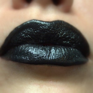 May include: Close-up of a person's lips with black lipstick. The lipstick has a glossy finish and is applied evenly.