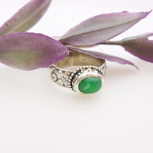May include: A silver ring with a green gemstone set in a floral design.