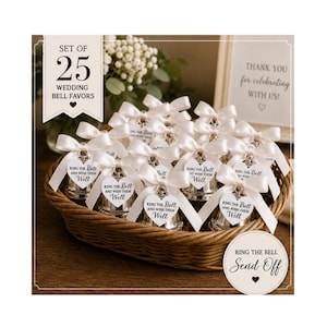 Peut inclure: Un ensemble de 25 clochettes de mariage argentées dans un panier en osier. Chaque clochette est ornée d'un ruban en satin blanc et d'une étiquette en forme de cœur avec le texte : Ring the bell and wish them well. Un panneau indique : Set of 25 wedding bell favors.