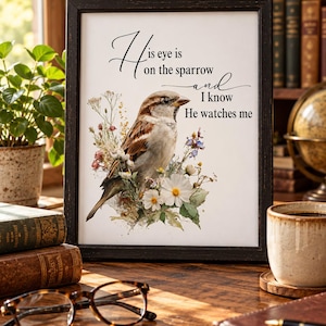 May include: A framed wall art print featuring a brown and white sparrow perched among colorful wildflowers. The text reads: His eye is on the sparrow and I know He watches me. The print is housed in a dark, distressed wooden frame.