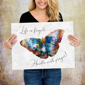 May include: A white poster with a colorful butterfly illustration and the text "Life is fragile... Handle with prayer!"