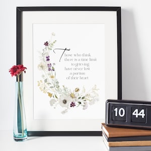 May include: A framed print with a floral design and the text "Those who think there is a time limit to grieving have never lost a portion of their heart." A red flower is in a blue vase. A black flip clock displays 10:44.