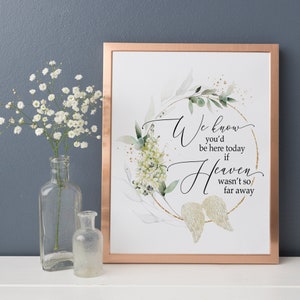 May include: A framed print with a watercolor illustration of a wreath of green leaves and white flowers with gold accents. The text reads "We know you'd be here today if Heaven wasn't so far away".