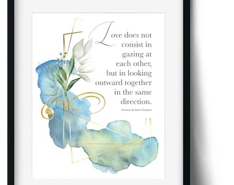 May include: A watercolour print with a blue and green background and gold accents. The print features a quote by Antoine de Saint-Exupery: "Love does not consist in gazing at each other, but in looking outward together in the same direction."