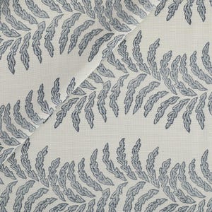 May include: Close-up of a white fabric with a repeating pattern of blue fern-like leaves. The leaves are detailed with dark blue outlines and fill the fabric in horizontal rows. The fabric is folded, showing the texture and design.