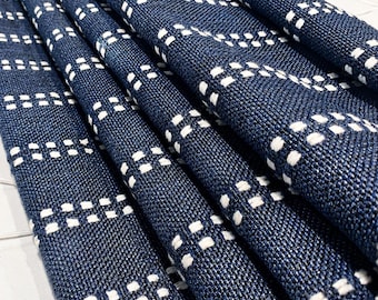 May include: Close-up of folded navy blue fabric with a repeating pattern of small white squares. The fabric appears to be a textured weave, possibly linen or cotton, with a subtle sheen. The design creates a geometric effect.