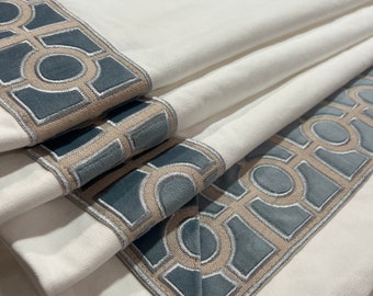 May include: White fabric window shade with a geometric pattern border in beige and blue. The border is made of a velvet-like material.