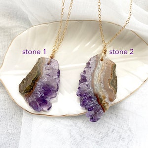 May include: Two gold chain necklaces with amethyst crystal pendants. The amethyst crystals are both a light purple color and have a natural, rough texture. The crystals are labeled "stone 1" and "stone 2".