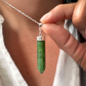 Könnte beinhalten: Eine silberne Kettenkette mit einem grünen Jade-Anhänger in Form eines langen, spitzen Kristalls.