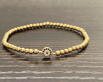 May include: A gold beaded bracelet with a blue and white evil eye charm.