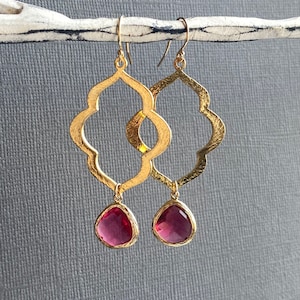 Op de afbeelding: Gouden oorbellen met een geometrisch ontwerp en roze druppelvormige stenen.