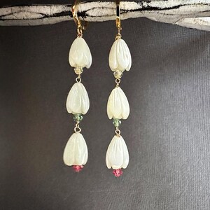 Könnte beinhalten: Ein Paar goldene Ohrringe mit weißen, blumenförmigen Perlen und grünen und rosa Akzenten.
