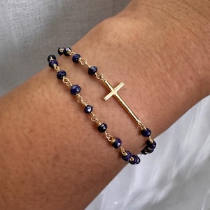 May include: A gold chain bracelet with a gold cross charm and dark blue beads.