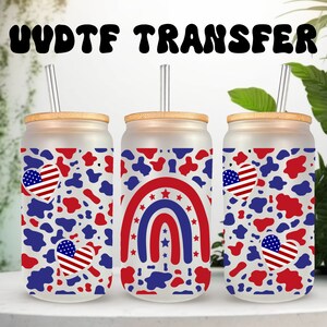 May include: Three clear glass tumblers with a white, red, and blue cow print design. Each tumbler has a different design: one has two red, white, and blue hearts, one has a red, white, and blue rainbow, and one has a red, white, and blue heart. Each tumbler has a bamboo lid and a clear straw.