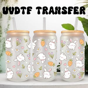 May include: Three frosted glass drinkware with bamboo lids and straws. Each glass is decorated with a repeating pattern of white bunnies, carrots, flowers, and hearts. The text "UVDTF TRANSFER" is at the top.