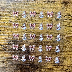Könnte beinhalten: Nagelkunst-Abziehbilder mit Schleifen im Leopardenmuster und Schneemännern mit Hüten. Die Schneemänner haben eine weiße Basis mit schwarzen Punkten und einen roten Schal. Die Schleifen haben einen rosa-braunen Leopardenmuster.