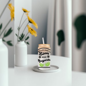 May include: A white can with a black and green design that says "When life gives you limes, make margaritas". The can has a straw sticking out of the top and is sitting on a white coaster.