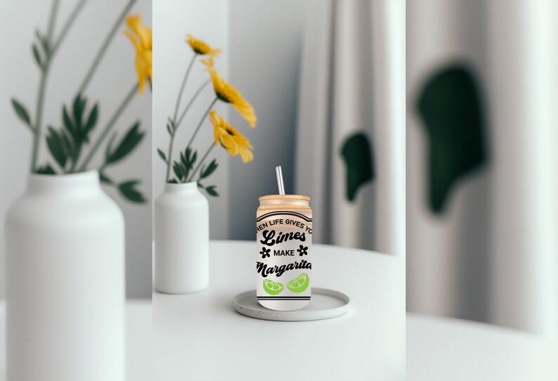 May include: A white can with a black and green design that says "When life gives you limes, make margaritas". The can has a straw sticking out of the top and is sitting on a white coaster.